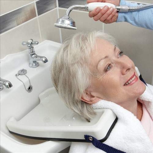 An image of a woman with the hair wash tray around her shoulders. She is sat with her back to the sink whilst someone is washing her hair. 