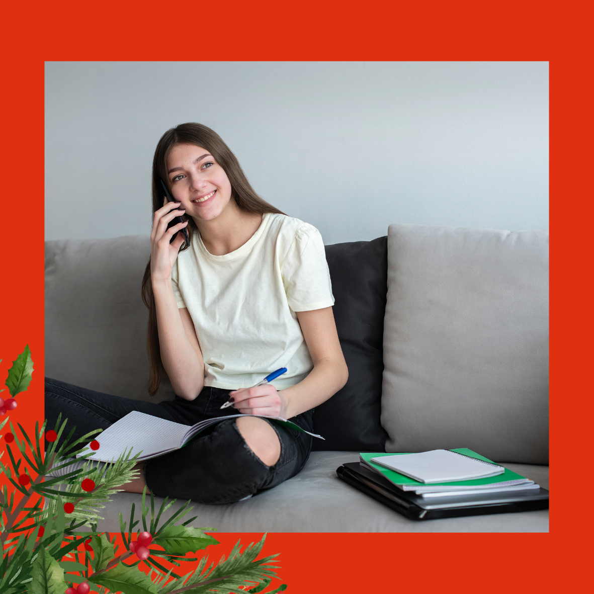 An image of a teenage girl, with long brunette hair, talking on the phone. She is using her other hand to make notes in a notebook and is sat crossed legged on a sofa. There is holly and berries in the left hand corner.
