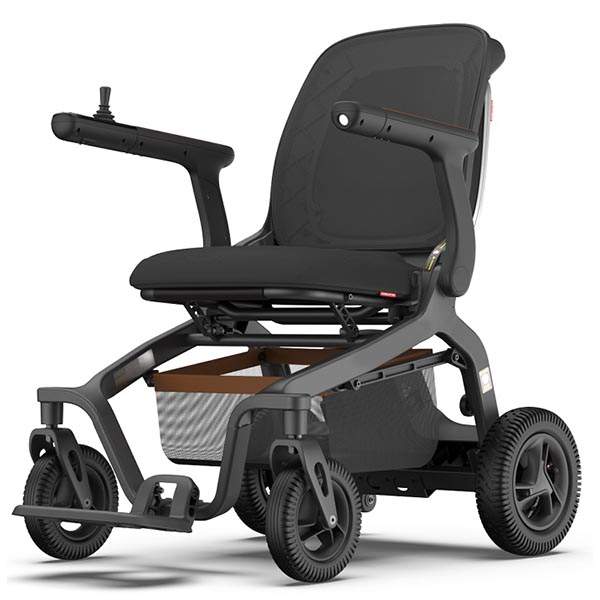 An image of the Light Electric Wheelchair, which is a cushioned black seat with two arm-rests with joysticks on each side. It has four black wheels, a foot rest and a storage basket underneath. 