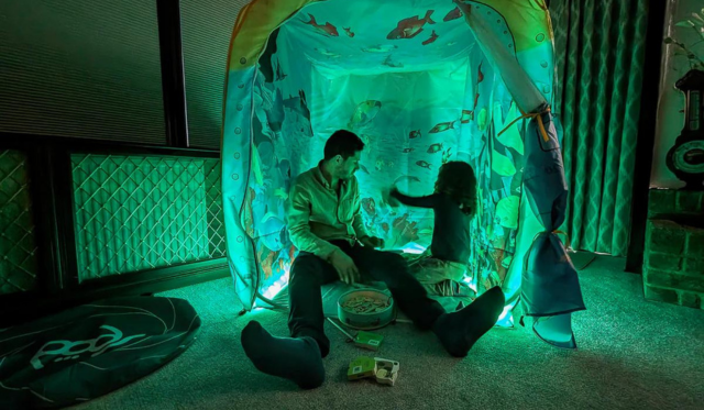 Adult and child playing inside an underwater themed pod with aqua lighting