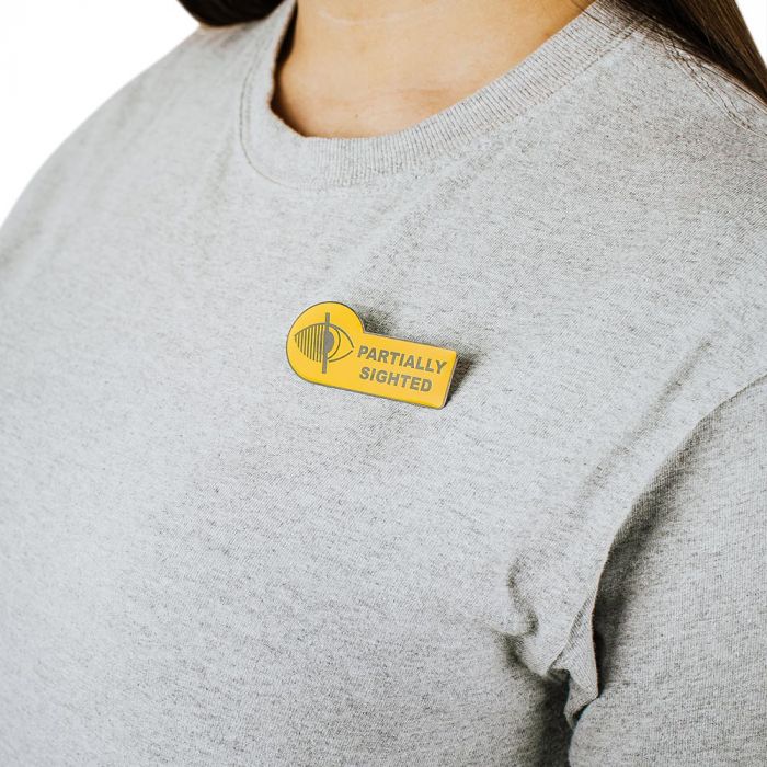 Yellow badge with partially sighted printed on it pinned to a person wearing a T-Shirt