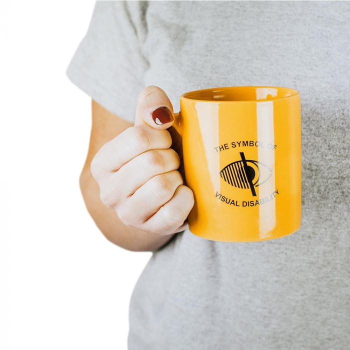 Person holding Bright yellow mug with the symbol of visual disability logo and text in centre