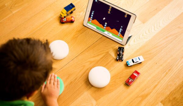 Child playing with the buttons, one of them lit up as he presses it, the ipad screen in front of him