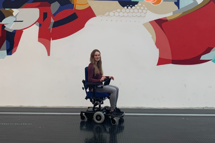 Girl in electric wheelchair in front of a painted wall 