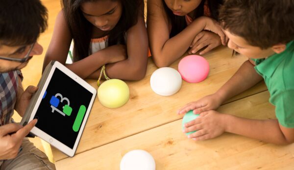 A group of children with the buttons, and a teacher showing them the ipad screen with a game on it