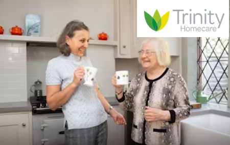 Trinity Healthcare logo above two people having a cup of tea and smiling.