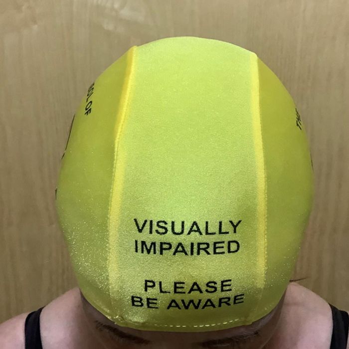 Luminous yellow swimming cap on persons head with visually impaired please be aware printed on front